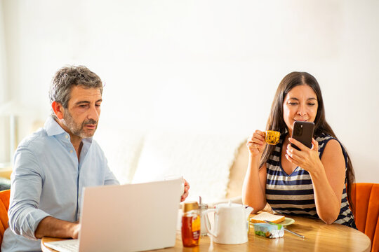 Couple having breakfast while working and checking phone at home