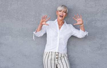 Scared adult woman, being terrible accident, against gray background - wall. Frightened middle age woman