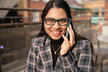Young woman in stylish outfit talking on phone outdoors in urban setting during sunny day