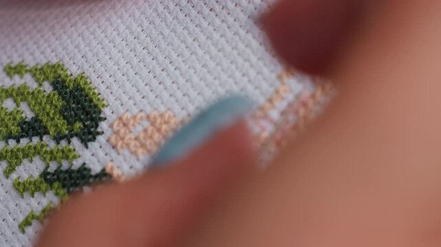 Extreme close up of skilled person embroidering colorful pattern on white fabric, delicate needlework forming tree like design with green and peach threads