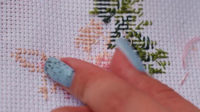 Extreme close up craft person cutting thread on embroidered fabric using metal scissors, blue nails visible while creating precise detail, showing patience and artistry