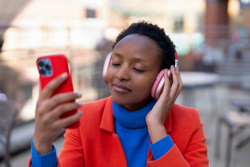 Young woman enjoys music while using smartphone in urban cafe setting