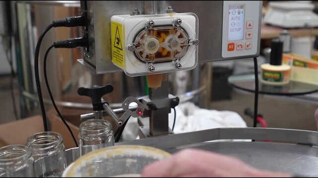 Cesis, Latvia - November 21, 2025: Skilled technician operates advanced filling machine, camera zooms in on precise hand movements and equipment details