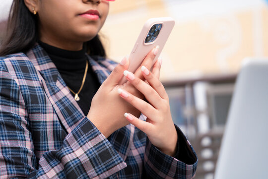 Young woman in formal wear uses smartphone while sitting in modern workspace