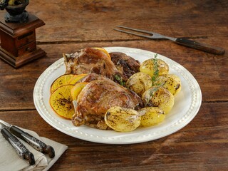 A beautifully arranged plate showcases tender roasted chicken, accompanied by golden potatoes and citrus slices. The rustic wooden table enhances the dish's inviting appeal