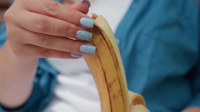 close up woman peeling plantain skin revealing fresh fruit, natural daylight emphasizing smooth yellow surface and soft texture, gentle motion of hands with light blue nail polish
