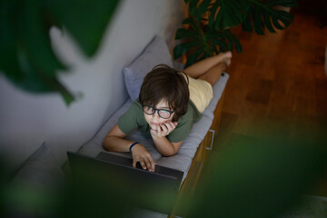 Child concentrating on laptop while lying down indoors