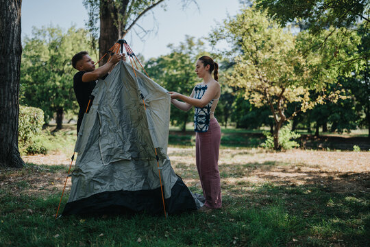 Two friends work together to pitch a tent in a bright park. The scene captures teamwork, outdoor activity, and the calm enjoyment of nature as they prepare shelter on a sunny day. - Powered by Adobe