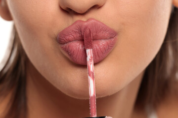 Close-up of a woman puckering lips while applying pink lip gloss, studio shot on a white background