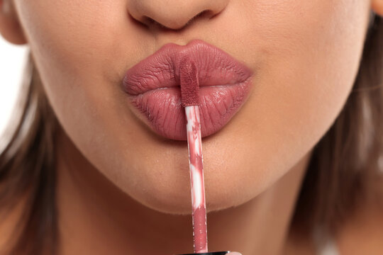 Close-up of a woman puckering lips while applying pink lip gloss, studio shot on a white background