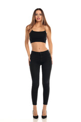 Fototapeta premium Full length studio shot of a tall brunette model with long straight hair wearing a black crop top, skinny jeans and high heels standing confidently on a white background