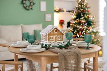 Festive table setting with beautiful gingerbread house against blurred lights indoors. Christmas atmosphere