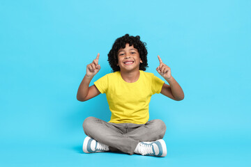 Portrait of little boy pointing on light blue background