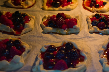 Close-up of warm berry tartlets filled with raspberries, cranberries and blueberries. Soft light highlights glossy crust and juicy berries, creating a cozy, inviting baking mood.