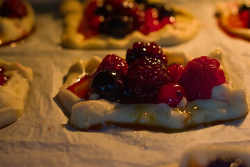 Close-up of warm berry tartlets filled with raspberries, cranberries and blueberries. Soft light highlights glossy crust and juicy berries, creating a cozy, inviting baking mood.