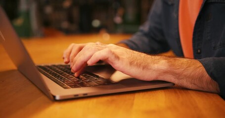 Close up of male hands typing on modern laptop keyboard while sitting at table in coworking space