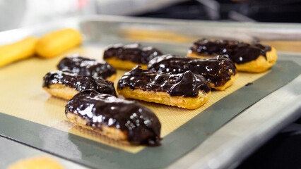 Freshly baked chocolate eclairs cooling on baking sheet