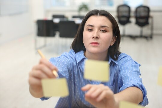 Woman writing on note near glass board in office - Powered by Adobe