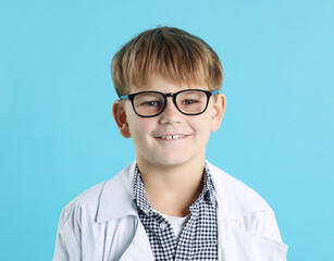 Smiling little boy in laboratory coat and glasses on light blue background. Child and science