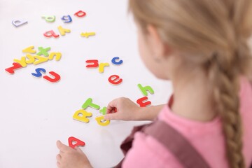 Little girl learning alphabet with letters at white table indoors, closeup