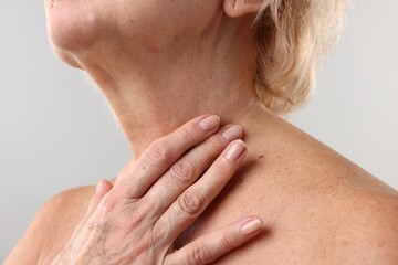 Senior woman touching her neck on light grey background, closeup
