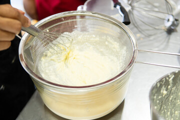 Hand sifting creamy mixture with whisk in kitchen
