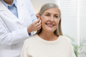 Obraz premium Doctor putting hearing aid into patient's ear in clinic, closeup