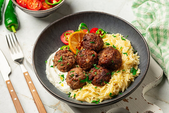 Greek Delicious beef meatballs -  Keftedes, or cutlets, made with origano, mint and lemon, served with orzo or risoni pasta and vegetables. White table. Homemade food.