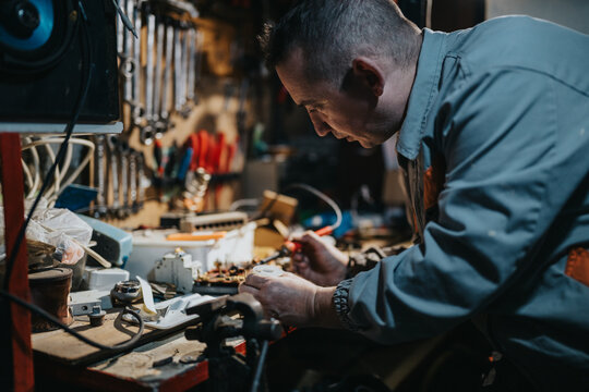 A skilled technician leans over a busy workbench filled with tools and electronic parts, carefully inspecting and repairing circuits with precision work in a crowded shop.