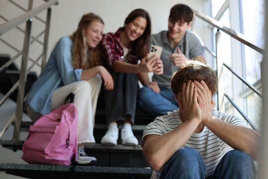 Students bullying their classmate on stairs indoors, selective focus