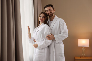 Happy couple wearing bathrobes near window in hotel room