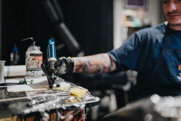 A tattoo artist wearing gloves uses a professional tattoo gun to outline and fill a design on a client's skin. Focus on tools, ink, and studio atmosphere.