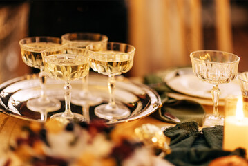 Elegant glassware filled with sparkling beverage arranged on a silver tray, surrounded by festive table settings, creating a warm and inviting atmosphere for celebration