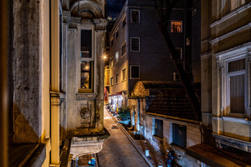 A quiet, steep cobblestone street in Beyoğlu at night, lit by window lights and a solitary shop, offering a peaceful escape from the bustling metropolis. Istanbul, Turkey.


