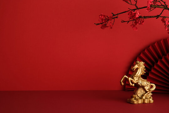 Golden horse statue next to a red folding fan on a red background with copy space. Happy Chinese New Year 2026, year of the fire horse.