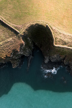 Aerial view of rugged cliffs meet the teal ocean, a stark contrast of earthy tones against the cool waters, St. Davids, Wales, United Kingdom.