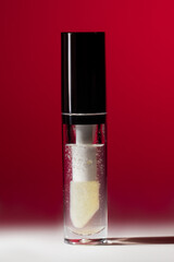 Transparent cosmetic serum bottle with soft applicator and bubbles on red background with copy space for skincare innovation, beauty branding and luxury cosmetic banner
