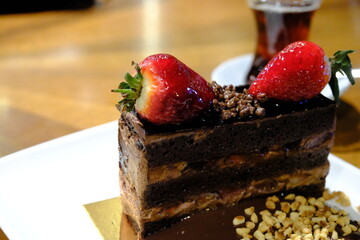 A close-up of a slice of fresh cake topped with strawberries. Tea next to a chocolate cake....