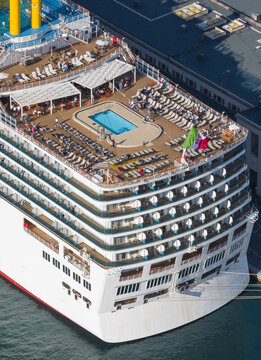 Aerial view of the ship's deck with a refreshing blue pool and rows of sunbeds, contrasting with the ship's white exterior, Trieste, Italy.