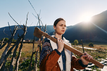 Fototapeta premium woman plank rural mountains fence sunlight portrait of young female carrying a wooden beam on her shoulder in countryside farm outdoor scene, rustic jacket and determined expression