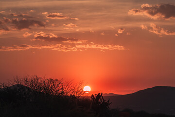 Intense orange sunset with bright sun over hills and nature in silhouette