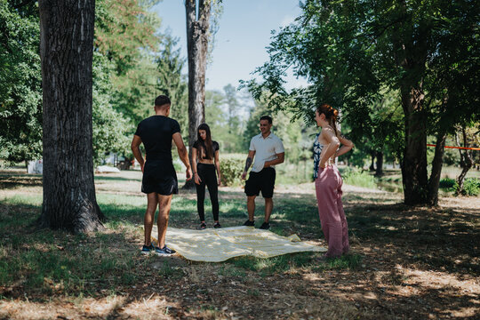 A diverse group of young adults gathers in a sunny park, chatting and bonding around a large striped mat. Casual outfits and relaxed poses convey friendship, leisure, and outdoor recreation.