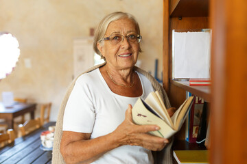 Senior woman smiling while holding a book in library