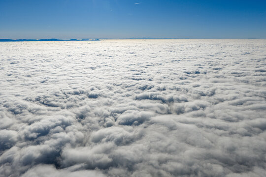 Aerial view of a sea of fluffy white clouds stretching to the horizon under a clear blue sky, Orschwiller, Grand Est, France.