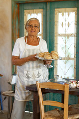 Smiling senior woman proudly presenting freshly baked bread rolls