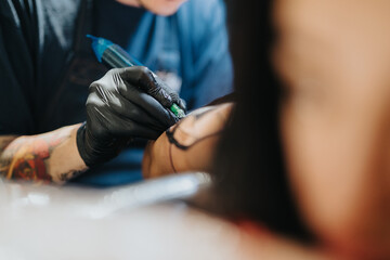 Obraz premium A tattoo artist in black gloves traces a design on a clients forearm using a tattoo machine in a studio setting.