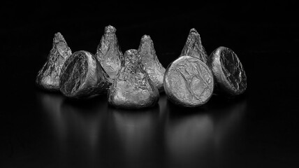Candies wrapped in aluminum foil on a black background. Black and white image.
