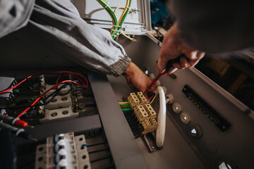 A technician wires a control panel, connecting terminals and cables inside an industrial cabinet.