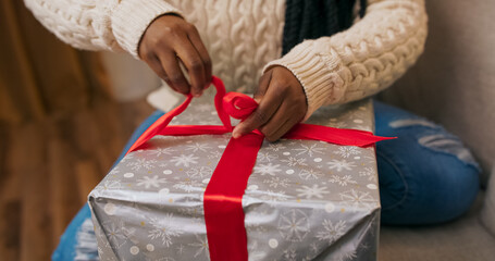 Preparing gifts for friends, a young woman of multi-racial background holds a gift in a close-up....