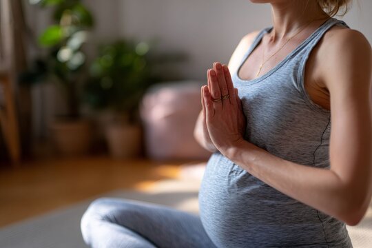 Pregnant woman practicing yoga meditation at home. Close up of female hands in prayer position near baby bump. Prenatal wellness and health concept
